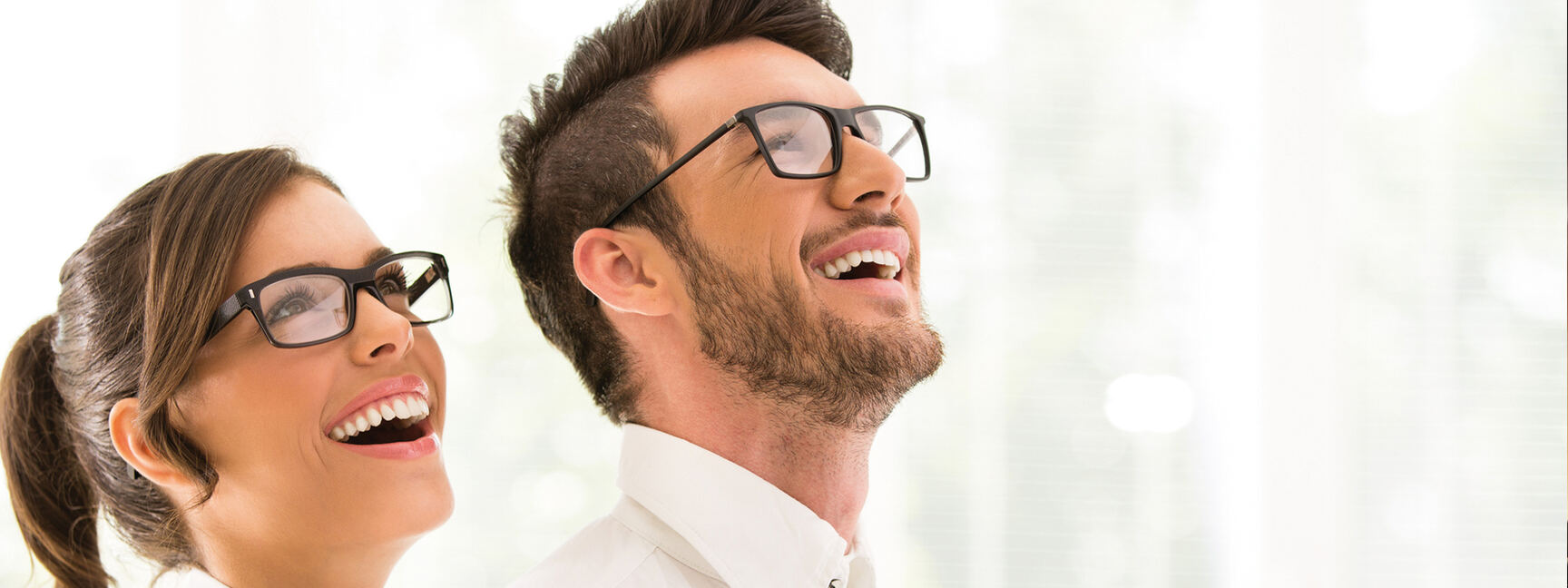 Eine Frau und ein Mann, die Brillen Tragen, blicken fröhlich nach oben 